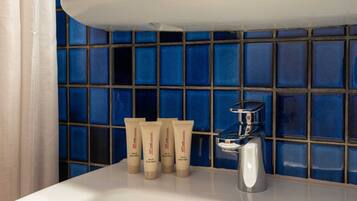 A bathroom with a white sink, a chrome faucet, and a blue tiled wall. There are three tubes of hair and body wash on the sink.