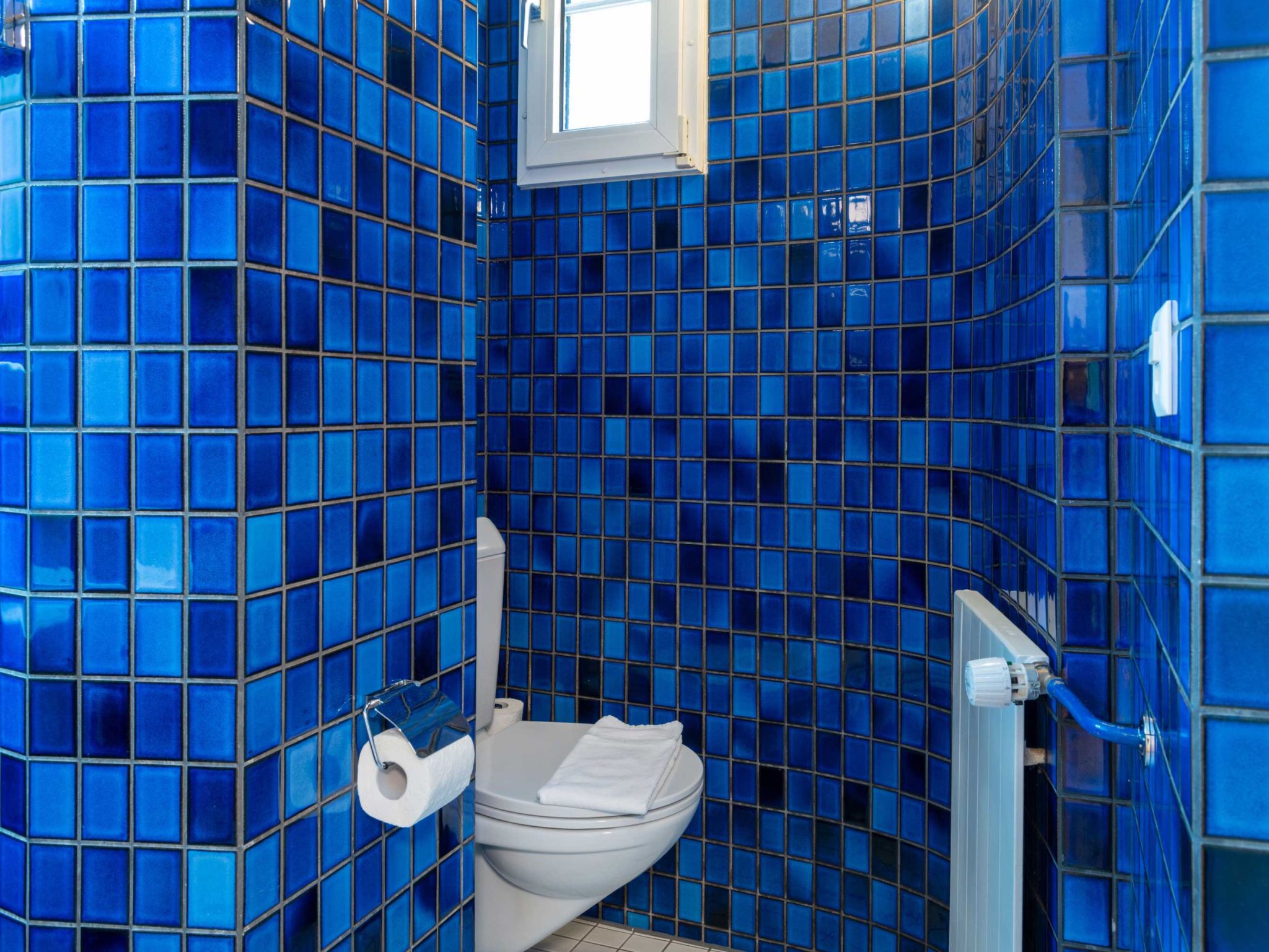 Un baño con paredes de azulejos azules y un inodoro blanco.