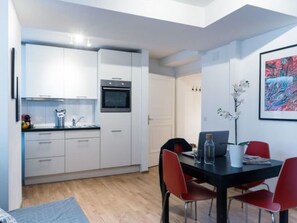 Une cuisine moderne avec des meubles blancs, un plan de travail noir et un coin repas comprenant une table noire et des chaises rouges.