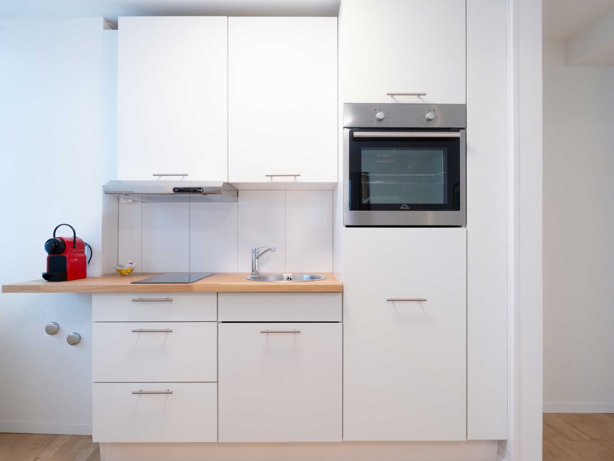 Eine moderne Küche mit weißen Schränken, einem Edelstahlbackofen und einer Holzarbeitsplatte.