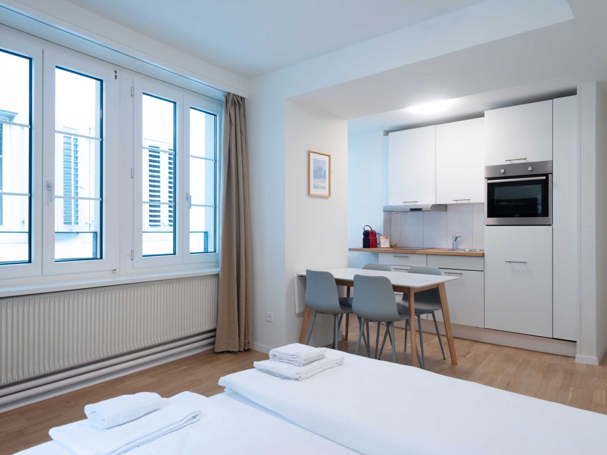 Una habitación de hotel moderna y funcional, con un ventanal grande, zona de comedor y kitchenette.