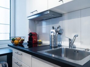 Une cuisine moderne avec un évier en acier inoxydable, un appareil électroménager rouge et un panier à fruits.