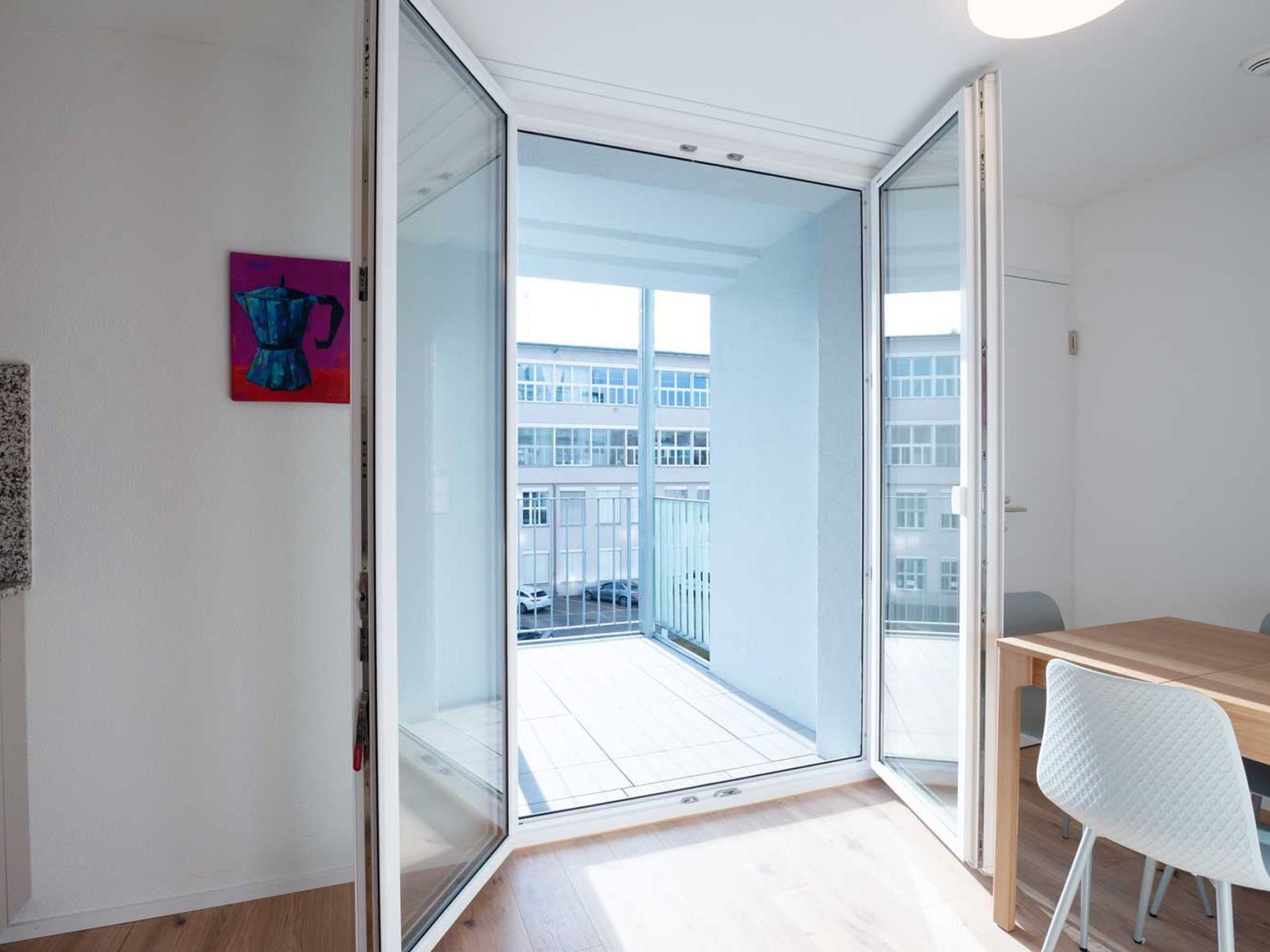 A modern room with a sliding glass door leading to a balcony, a wooden table, and a white chair.