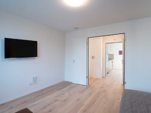 Ein Zimmer mit einem an der Wand befestigten Flachbildfernseher, Holzboden und einer Tür zu einem anderen Raum.