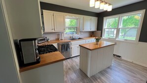 A modern kitchen with white cabinets, a built-in stove, a dishwasher, and a large window providing a view of the outdoors. - 1-4 Guests, 1 Bath Farm Stay at a Pygmy Goat Farm in Byron Center, Michigan (Byron Center)