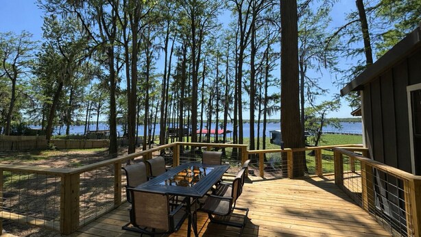Eine Holzterrasse mit Tisch und Stühlen, mit Blick auf einen See mit Bäumen.