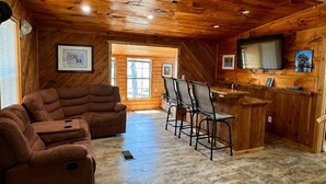 Ein Holzblockhaus-Interieur mit Wohnbereich, einer Küche mit Barhocker und einem Fernseher.