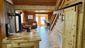 Ein Holzinterieur mit Kamin, einer Couch, einem Esstisch und einer Treppe.