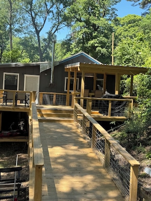 A wooden deck leading to a building with a covered porch, surrounded by trees.