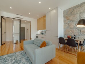 Ein modernes Wohnzimmer mit einer Couch, einem Essbereich mit Stühlen, einer Küche und einer Steinwand.
