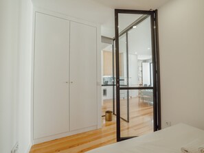 A room with a wooden floor, a white wardrobe, and a glass door leading to a kitchen area. - Apartment  by Interhome (Porto)