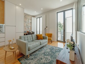 Ein modernes Wohnzimmer mit einem grauen Sofa, einem gelben Sessel, einem Esstisch und einem großen Fenster mit Blick ins Freie.