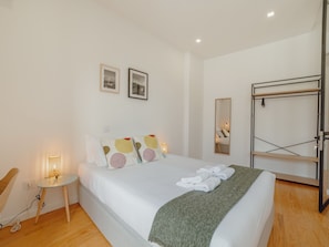 Ein Schlafzimmer mit Bett, Nachttisch mit Lampe, Spiegel und Kleiderschrank.