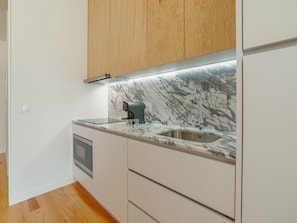 A modern kitchen with a built-in oven, a coffee machine, and a sink with a marble backsplash. - Apartment  by Interhome (Porto)