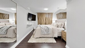 A modern bedroom with a large mirror, two beds, a TV, and a wardrobe. - Chic 2BR Suite Stylish Stay w/ Kitchen + Free Parking (Pickering)