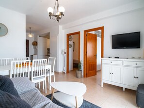 Una sala moderna con sofá, mesa de comedor, sillas, televisor y área de cocina con armarios y lavamanos.