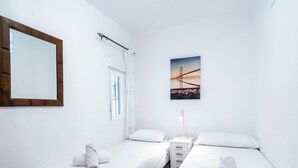 A bedroom with two single beds, a nightstand, a lamp, a window with curtains, a wall-mounted mirror, and a picture of a bridge. - Capri Sunset by Casasol by Interhome (Nerja)