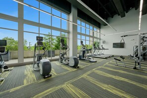 Ein Fitnessraum mit Trainingsgeräten, großen Fenstern und Blick auf Grünflächen.