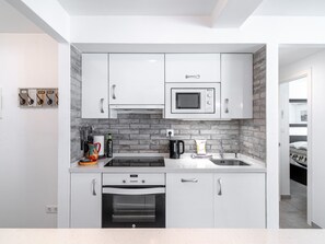 A compact kitchen with white cabinets, a microwave, a stove, and a sink. - Apartamento Urban Suite by Casasol by Interhome (Nerja)