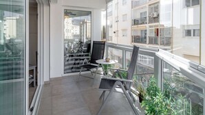 En balkon med glasdør, et lille bord, to stole og potteplanter.