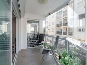 Ein Balkon mit Glastür, einem kleinen Tisch, zwei Stühlen und Pflanzen in Töpfen.