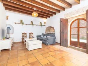 Una sala de estar acogedora con un sofá, una mesita y sillas. Se aprecia una pared de piedra y una puerta de madera con un ventanal.