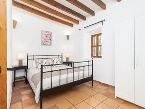 A bedroom with a bed, bedside tables, a nightstand, a wall-mounted lamp, a framed picture, a window, and a wardrobe. - Finca Can Nin by Interhome (Santanyí)
