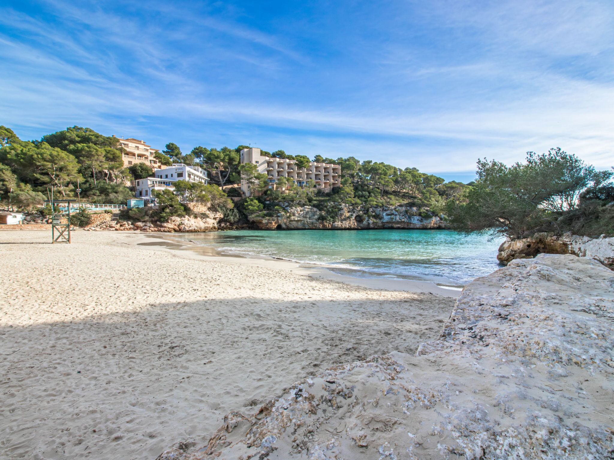 A beach with clear turquoise water, sandy shore, and buildings in the background.