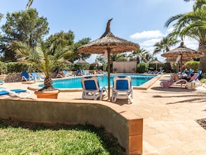 Un área junto a la piscina con sillas de descanso, piscina e palmeras.