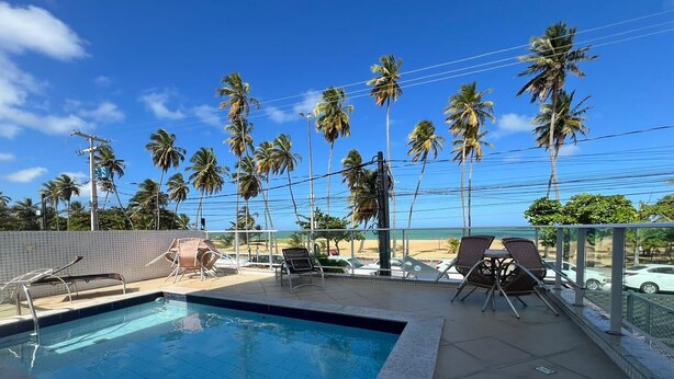 A swimming pool with lounge chairs and a view of the beach. - Clócio 201 - Beachfront apartment on Cabo Branco beach (João Pessoa)