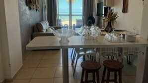 A modern kitchen with a dining area, a sofa, and a view of the outdoors. - Clócio 201 - Beachfront apartment on Cabo Branco beach (João Pessoa)