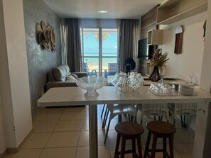 A modern kitchen with a dining area, a sofa, and a view of the outdoors. - Clócio 201 - Beachfront apartment on Cabo Branco beach (João Pessoa)