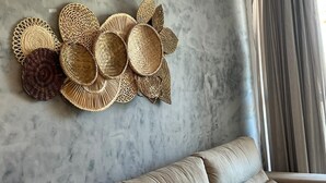 A wall with woven baskets and a sofa in a room with a marble wall and a window with curtains. - Clócio 201 - Beachfront apartment on Cabo Branco beach (João Pessoa)