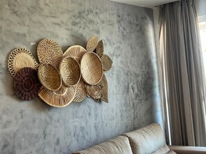 A wall with woven baskets and a sofa in a room with a marble wall and a window with curtains. - Clócio 201 - Beachfront apartment on Cabo Branco beach (João Pessoa)
