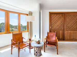 A room with two leather chairs, a small round table with a bottle and glasses, a floor lamp, and a view of greenery through large windows. - Villa Redonda by Interhome (Santanyí)