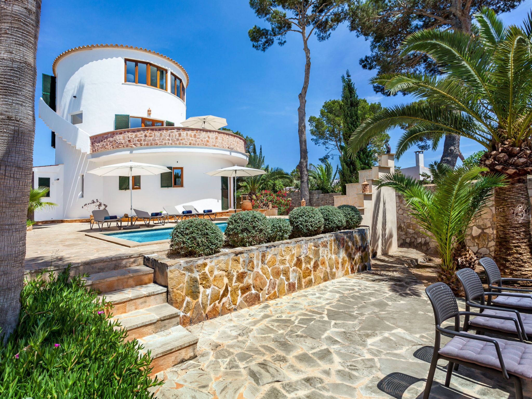 A modern villa with a pool, outdoor seating, and a stone wall.