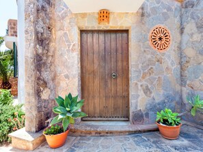 A stone wall entrance with a wooden door, potted plants, and a decorative metal piece. - Villa Redonda by Interhome (Santanyí)