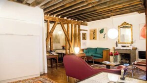 A rustic room with exposed wooden beams, a green sofa, a red armchair, a fireplace, and a mirror on the wall. - Royal Place des Vosges, 2nd floor, 4 guest, Old World Charm (Paris)