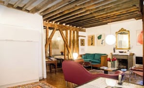 A rustic room with exposed wooden beams, a green sofa, a red armchair, a fireplace, and a mirror on the wall. - Royal Place des Vosges, 2nd floor, 4 guest, Old World Charm (Paris)