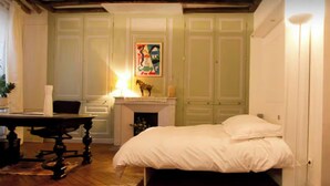 A bedroom with a bed, a desk, a chair, a fireplace, and a painting on the wall. - Royal Place des Vosges, 2nd floor, 4 guest, Old World Charm (Paris)