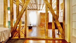 A room with exposed wooden beams, a wooden floor, a bed with a metal frame, and a window with curtains. - Royal Place des Vosges, 2nd floor, 4 guest, Old World Charm (Paris)