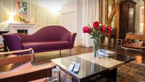 A modern living room with a purple sofa, a glass coffee table, and a vase of red flowers. - Royal Place des Vosges, 2nd floor, 4 guest, Old World Charm (Paris)