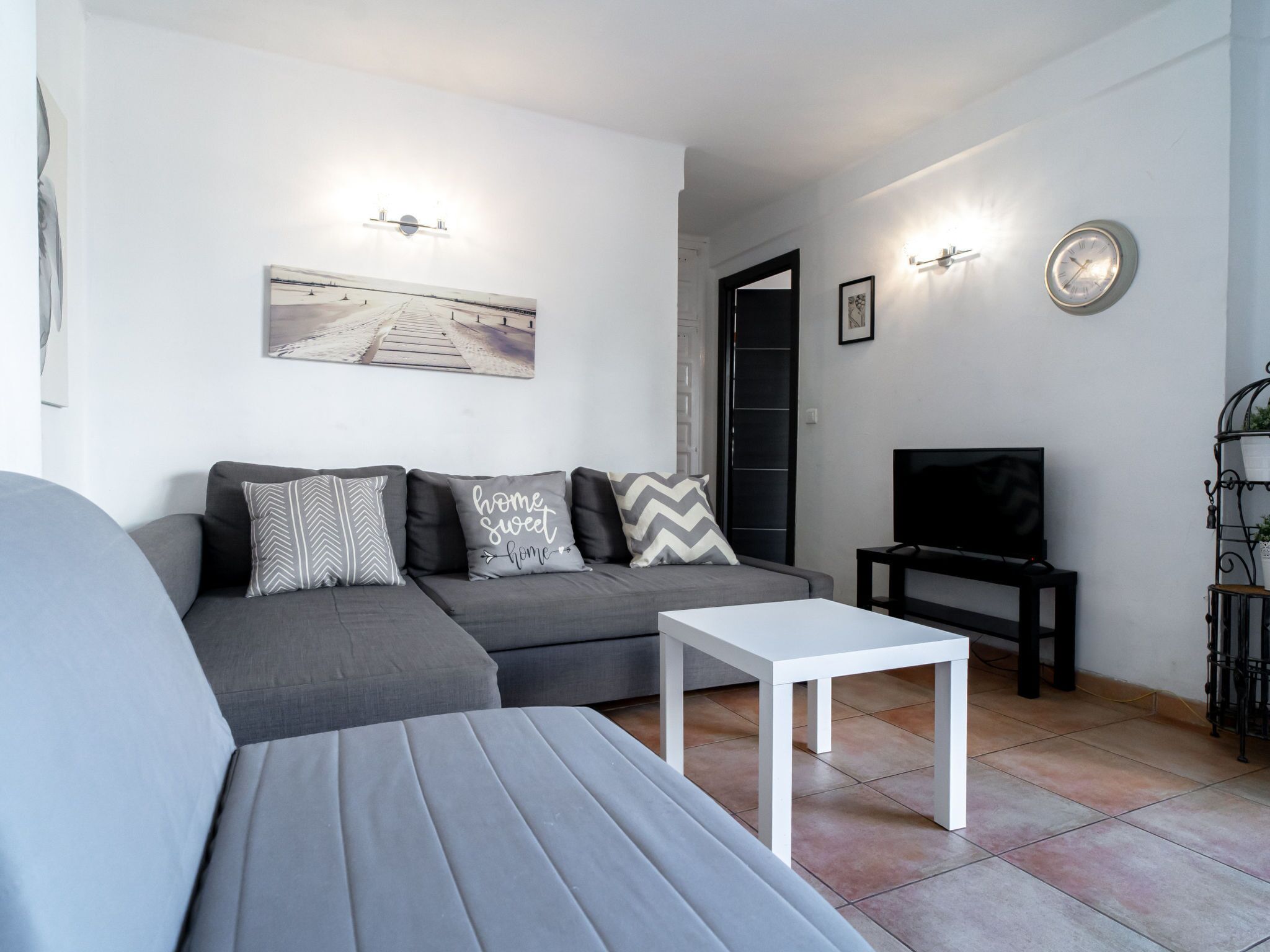 Una sala de estar moderna con un sofá gris, una mesa de centro blanca, un televisor de pantalla plana y un cuadro en la pared.