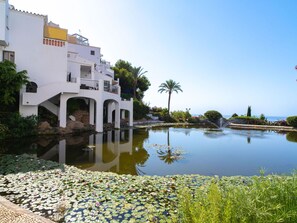 A serene waterfront property with a reflective pond, a white building with balconies, and lush greenery. - Capistrano Playa 116 by Casasol by Interhome (Nerja)