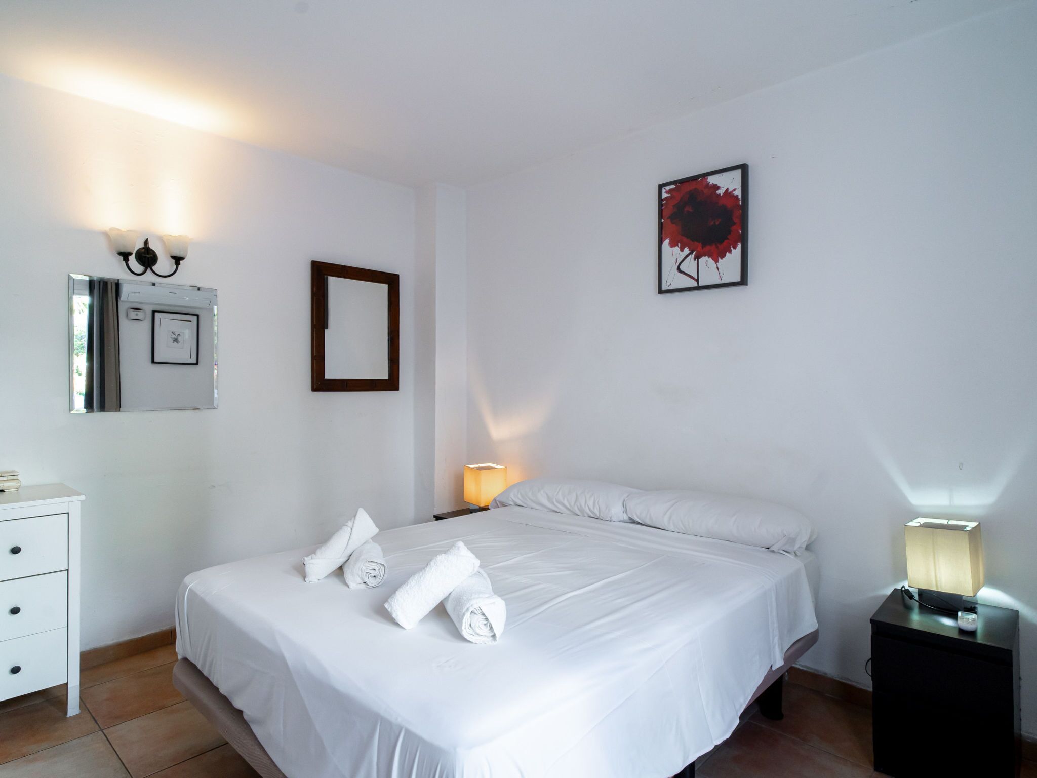 Ein Hotelzimmer mit Bett, Nachttisch, Lampe, Spiegel und einem gerahmten Bild an der Wand.