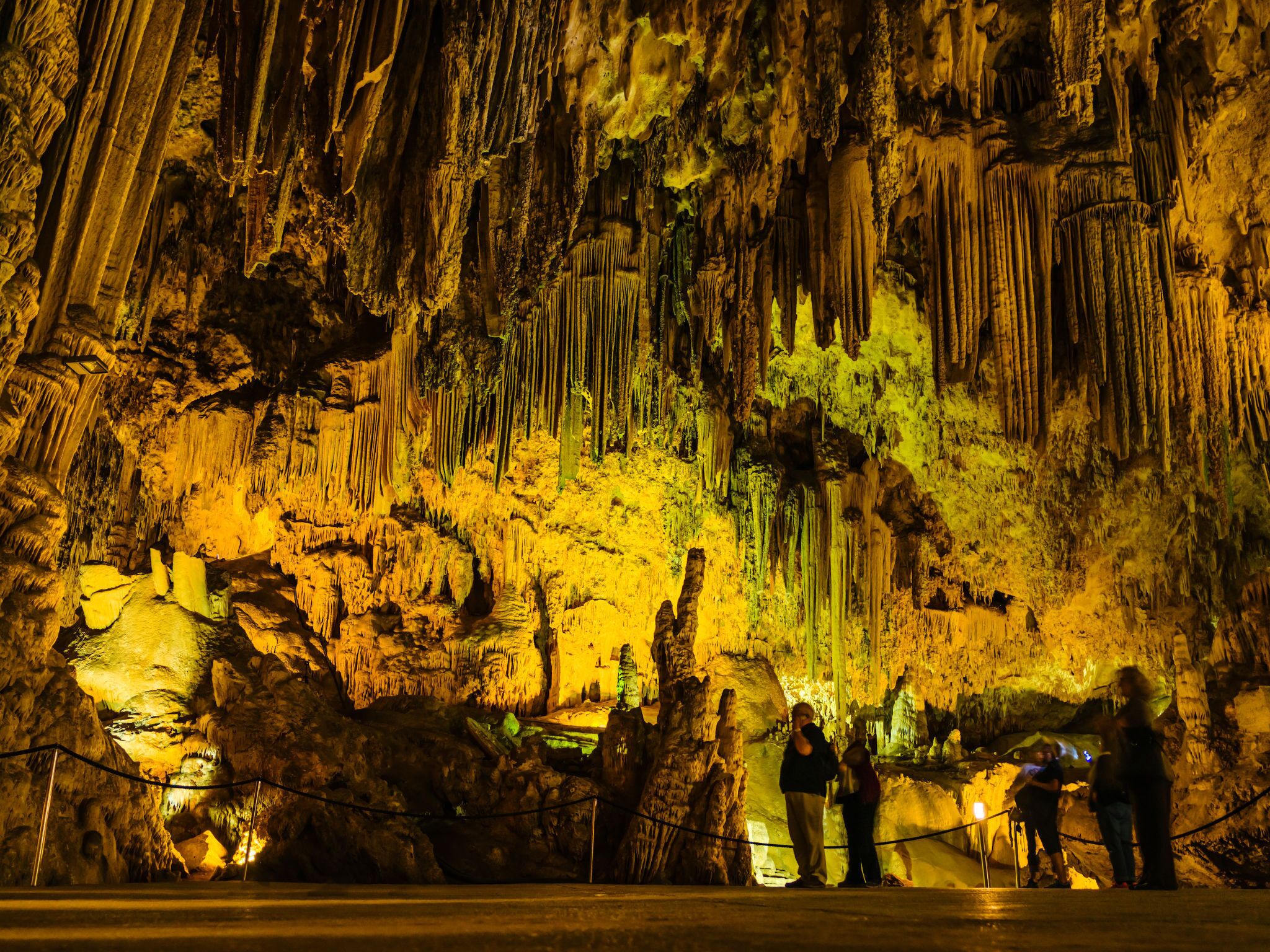 A cave with stalactites and stalagmites, illuminated by artificial lighting.
