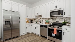 A modern kitchen with white cabinets, stainless steel appliances, a marble backsplash, and a wooden floor.