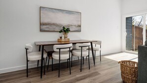 A dining area with a wooden table and four chairs, a painting on the wall, and a wicker basket.