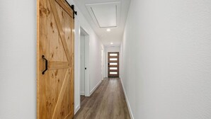 A hallway with a wooden door, white walls, and a wooden floor.