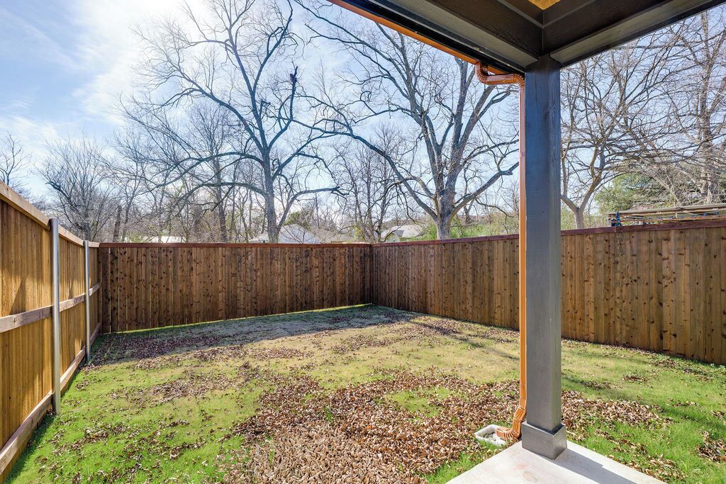 Ein überdachter Patio-Bereich mit Holzzaun, einer Metallstütze und Blick auf kahle Bäume.